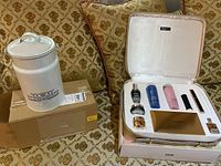 Photo showing the Lancome gift set box open with multiple skincare and cosmetic items inside, and the white ceramic Beekman tin on top of a brown shipping box.
