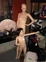 Photo showing two female mannequins and one child mannequin standing in basement surroundings with various items around them, one female mannequin with hand on hip.