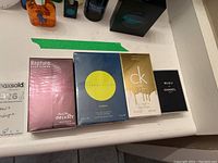 Overview of four sealed cologne boxes: Shirley May Deluxe Rapture, Perry Ellis Citron, CK Gold, Bleu de Chanel.