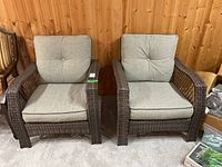 Front view of two brown synthetic wicker armchairs with grey cushions