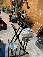 Photo showing several black metal speaker stands grouped in a room, some with X-frame designs and others with triple vertical supports.