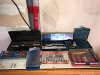 Wide shot of multiple socket sets, screwdriver bit sets and nut drivers arranged on a white surface showing different brands and packaging conditions