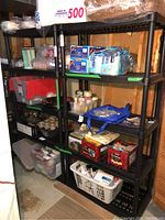 Full view of two black plastic utility shelving units with various household items on shelves.