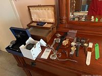Full lot display of watches and jewelry on wooden dresser with jewelry box open.
