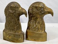 Pair of brass eagle head bookends side by side showing front and side profiles.