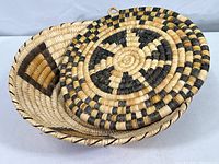 Woven basket with nested cover or hot pad showing concentric circle pattern in natural, black, and brown fibers