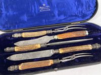 Three-piece matched Mappin & Webb carving set including knife, fork, and sharpening steel with wooden handles and ornate metal ends, displayed in original blue velvet-lined case.