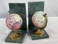 Front view of the pair of marble and metal globe bookends showing the globes mounted on polished green marble L-shaped bases with brass-tone stands.