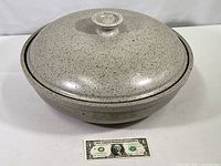 Full view of covered stoneware bowl with speckled gray finish and dollar bill for scale.