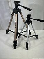 Two Velbon camera tripods side by side: Larger model CX 690 and smaller model CX 200 with telescoping legs and black tripod heads.