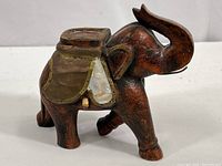 Side view of wood elephant showing metal and organic material saddle and detailed wood grain.