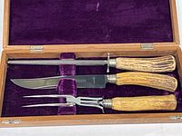 Three-piece carving set in wooden box lined with purple velvet, including knife, fork, and sharpening steel with wooden handles