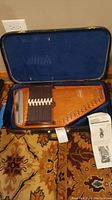 Photo showing the autoharp inside the hard case with blue interior lining, displaying the chord bars and strings.