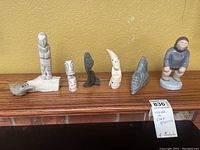 Full display of six carved stone and ceramic ethnic figurines on wood surface against a yellow textured wall.