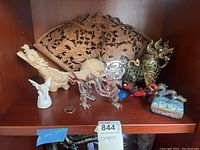 Overview of multiple Chinese dragon-themed items including carved wooden figures, a carved wooden panel, glass dragon, metal dragon, painted dragon figurine, and cloisonne musical trinket box, arranged on a wooden shelf.