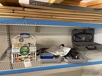 Shelf with Dremel tool accessory kit and multiple gray tool cases with manuals and cords.