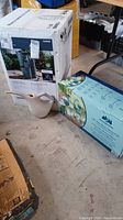 Photo of ceramic watering can, packaged Blue Heron figures box, and the boxed fountain package in garage setting.
