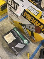Photo showing boxed Central Pneumatic framing nailer and box of Hitachi nails on shop floor.