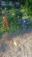 Outdoor setting with metal giraffe and elephant sculptures on gravel, surrounded by plants.