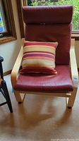 Front view of the Ikea Poäng chair showing burgundy leather cushion and striped throw pillow.