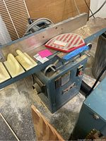 Front and left side view showing infeed and outfeed cast iron tables, red cutter head guard, white plastic push blocks on table