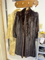 Two full-length mink coats hanging side by side on a coat rack: one dark brown and one light tan.