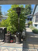 Full view of the Fire Sense patio heater standing beside a storage unit on a patio, showing the overall height and design.