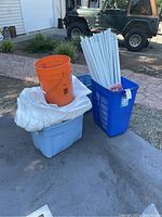 Full view of party tent parts grouped outside including buckets, poles, fabric cover