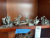 Collection of eight pewter dragon figurines displayed on wooden shelves including dragons with castles, different poses, and a globe object.