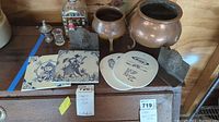 Overview of the lot showing copper pots, ceramic tiles, metal bookends, and decorative decanter