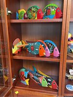 Overview of three shelves inside a wooden cabinet containing multiple hand painted wooden fish figures in different sizes and colors