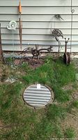 Four metal yard art pieces - bird, snail, dragonfly sculptures, and a round metal framed mirror shown against a siding wall outdoors.
