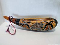 Side view of the guiro showing intricate carved floral and turtle designs in natural wood color and black paint.