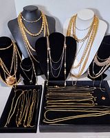 Photo showing a variety of gold tone fashion necklaces on black and white displays, some multi-strand and beaded.
