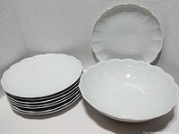 Eight stackable ribbed and scalloped white plates along with one large serving bowl visible on a white surface.