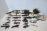 Overview of all vintage GI Joe toy accessories spread out, showing various toy guns, rifles, sword, flamethrower, and gear.