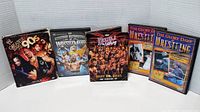Five DVD cases displayed standing showing front cover art of wrestling DVDs from various series.