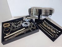 Photo showing multiple bracelets including rhinestone bangles, grey and silver bead bracelets, gold-tone and silver-tone chain link bracelets, and a wide cuff bracelet with braided metal design and round bead accents.