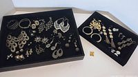 Overview of multiple pairs of pierced silver tone and rhinestone costume earrings in black display trays.