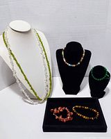 Two long chip bead necklaces shown on white display bust and table; green peridot and clear quartz stones visible