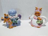 Front angled view of both ceramic figural teapots showing the Humpty Dumpty teapot and Bunny Brunch bunny teapot with detailed colors and shapes