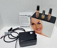 Luminess airbrush system packaging with 3 small sealed liquid foundation bottles, registration card, and air compressor with hose and gun