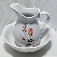 Front view of the ceramic water pitcher showing a floral rose design with leaves, placed inside the scalloped basin.