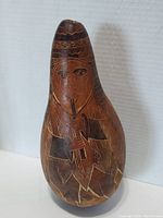 Front view of the hand-carved gourd flute player with detailed etched patterns and brown-black natural coloring.