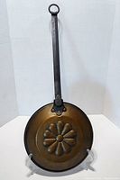 Front view of the copper hearth pan showing the cast iron handle and embossed floral design on base.