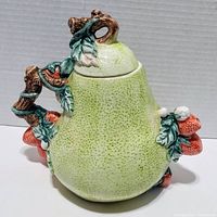 Side view of vintage pear-shaped ceramic teapot with strawberry accents, lid on top