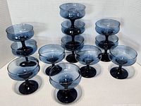 Twelve blue glass wine coupe glasses arranged in stacks and rows, showing the full set and individual pieces.
