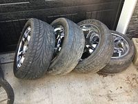 Set of four chrome 20-inch wheels with tires placed on ground showing outer side of wheels and tread wear on tires.