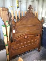 Full view of disassembled antique solid wood bed headboard with carved floral/leaf motif, finials, and recessed panels in medium wood finish.