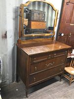 Full view of the antique dresser with attached mirror, showing the front and right side, including the detailed woodwork and the mirror's wooden frame.